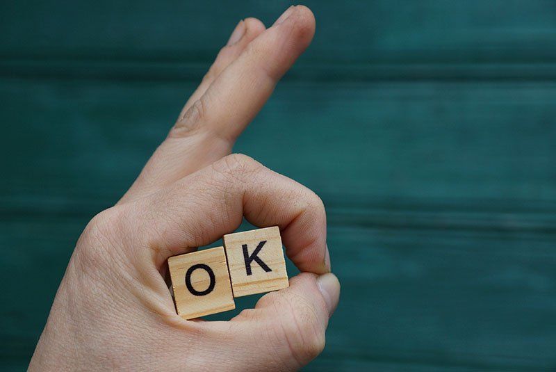 Hand Gesture And Wooden Letters With The Word Ok On A Green Back