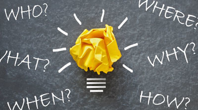 A screwed up ball of yellow paper against a blackboard is turned into a lit light bulb with white chalk.