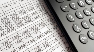 A populated financial ledger sheet undearneath a calculator.