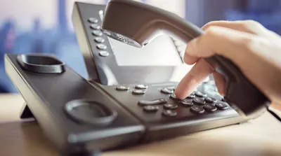 A hand dialing numbers into an office phone.