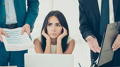 An unhappy business woman being shown wads of documents by two colleagues on her left and right.